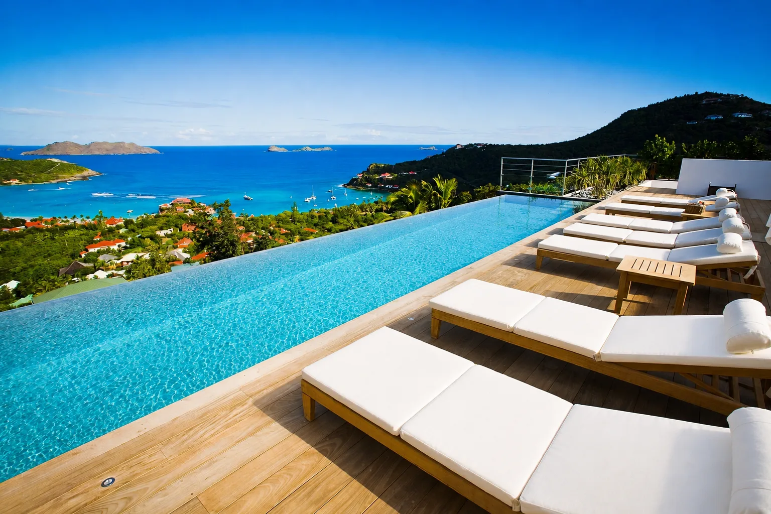 Infinity pool and teak deck lined with sun loungers above St. Jean Bay and the Caribbean Sea